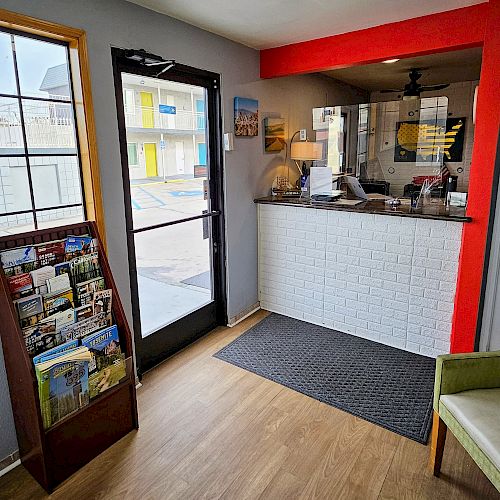 The image shows a small office or reception area with a chair, brochure stand, window, door, and a counter with a red frame and lamp.