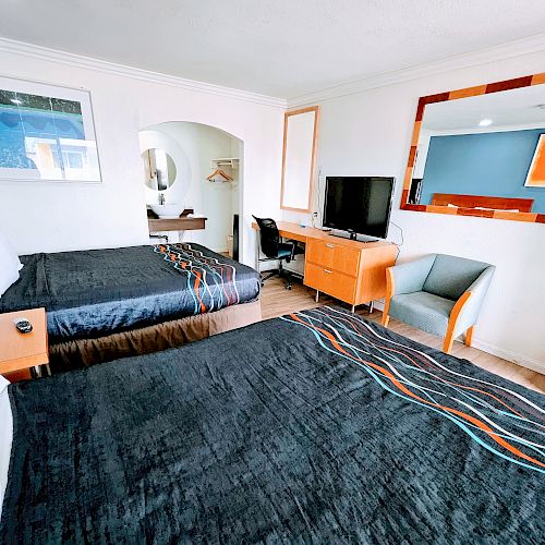 This image shows a hotel room with two beds, a TV, a desk, a chair, and a large mirror above the desk.