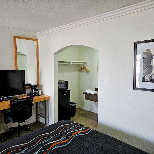 The image shows a hotel room with a bed, desk with a chair, TV, and a bathroom with a tub, towels, and a mini-fridge. Modern decor is present.