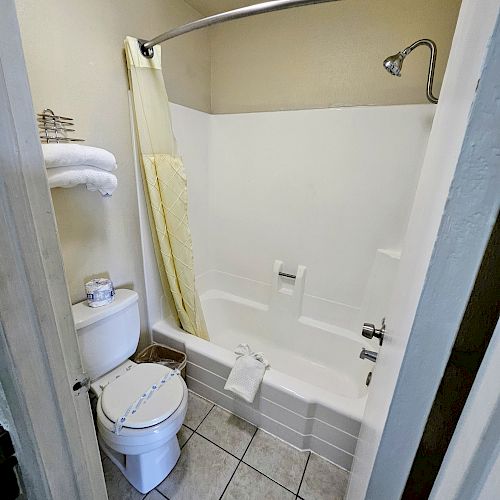 A bathroom with a bathtub-shower combo, a toilet, towels on a rack, and a shower curtain partially drawn. The floor is tiled.