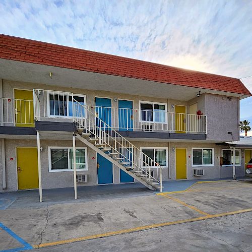 A two-story motel with colorful doors, exterior staircases, and a parked car in the lot. There's a handicap parking space marked in blue.